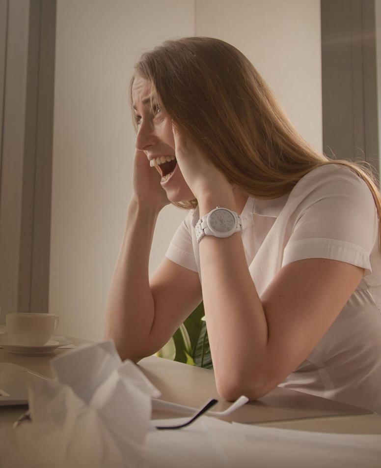 γυναίκα σε γραφείο εργασίας, απογοητευμένη και παρουσιάζοντας σημάδια burnout, με χαρτιά και άδεια φλιτζάνια καφέ γύρω της.